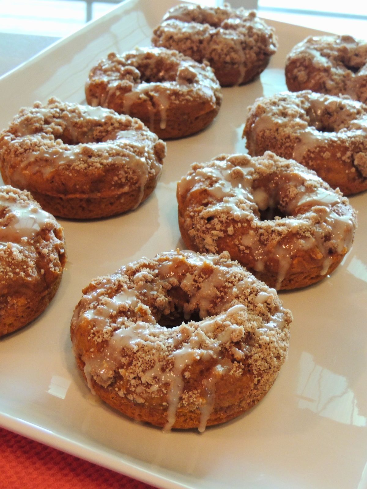baked pumpkin donuts with crumb topping and glaze on white platter.