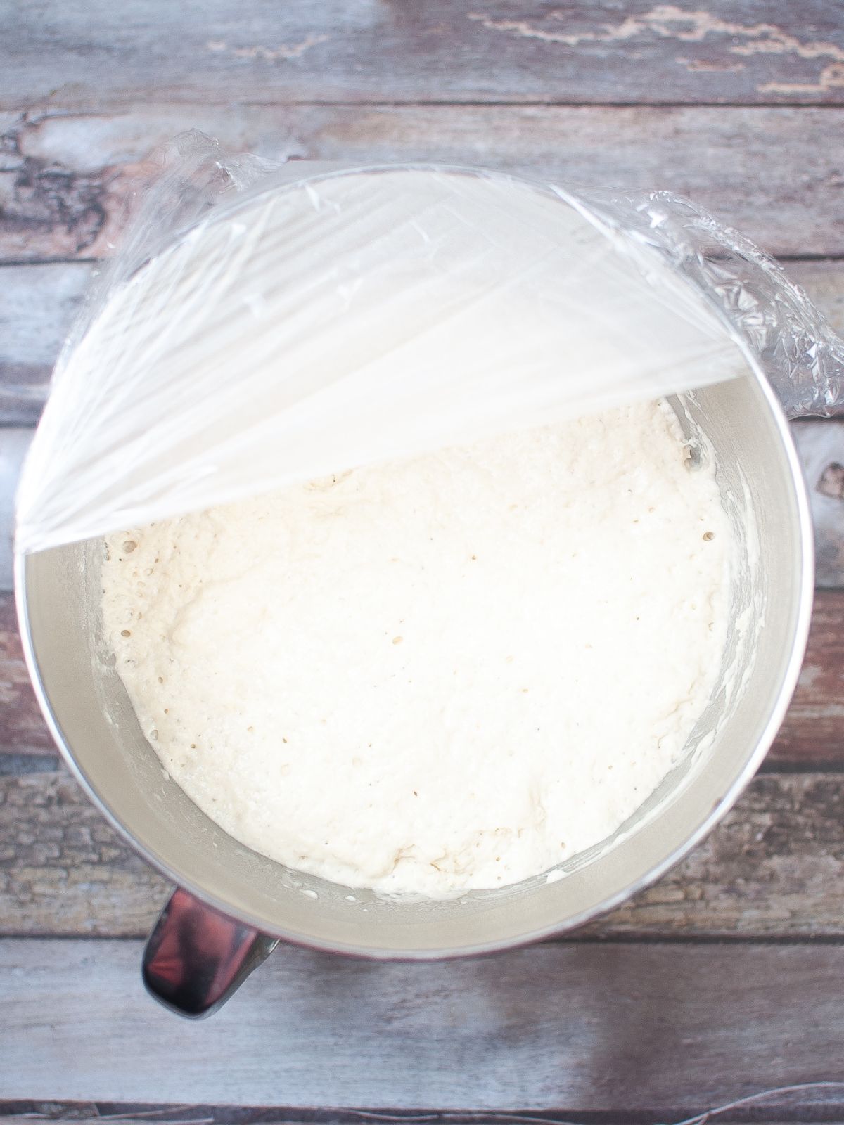 bread dough in large bowl with plastic wrap over half of the bowl.