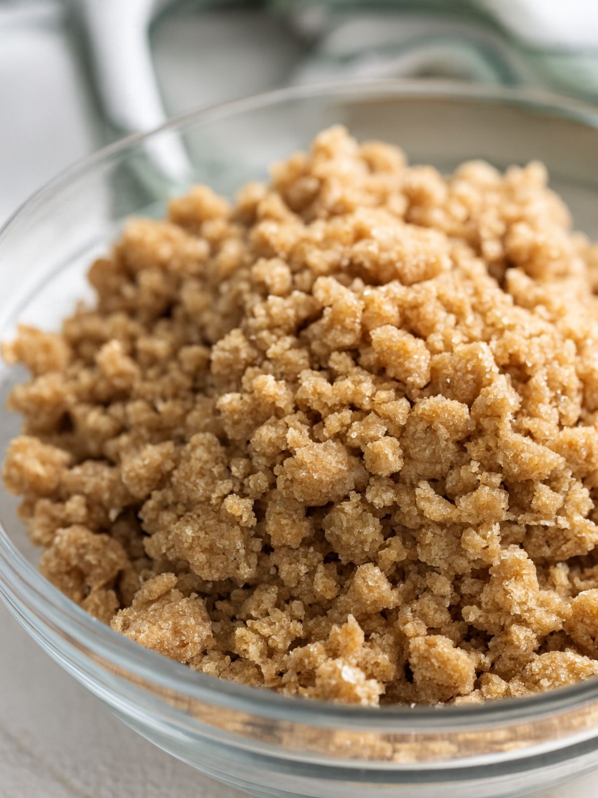 Glass bowl filled with crumb topping made from brown sugar, flour, butter, and oats, ready to use for baking pumpkin glazed donuts.