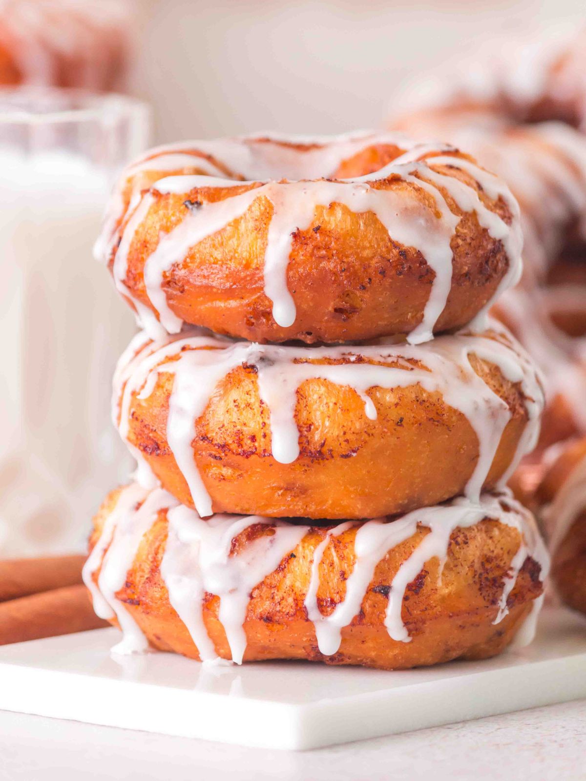 Stack of 3 cinnamon roll donuts with glazed drizzled on.
