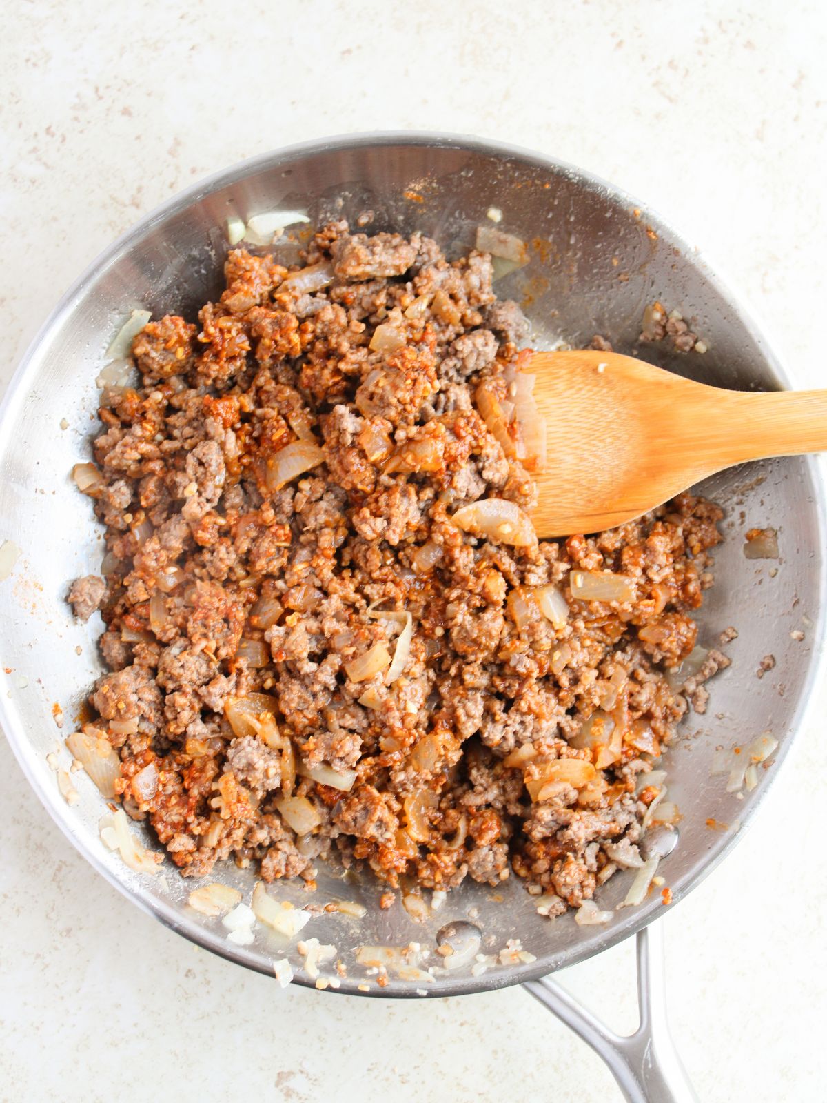 cooked and seasoned ground beef in skillet with wooden spoon.
