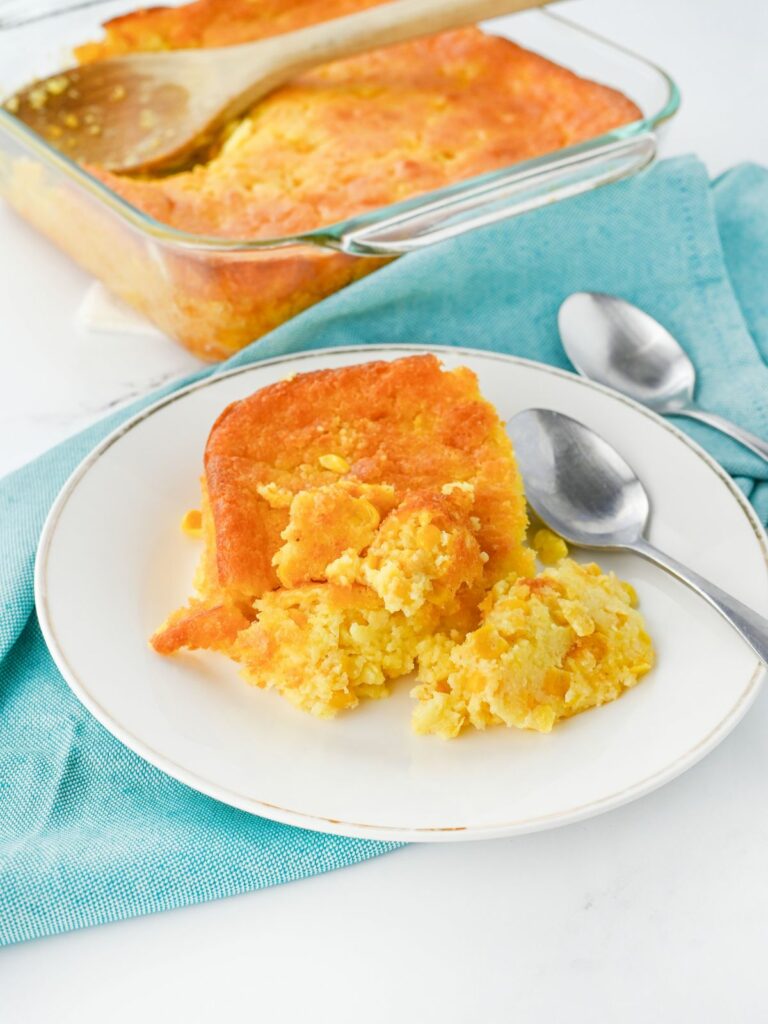 Jiffy Corn Bread Pudding Casserole served on a white dish with the rest in the baking dish in the background.