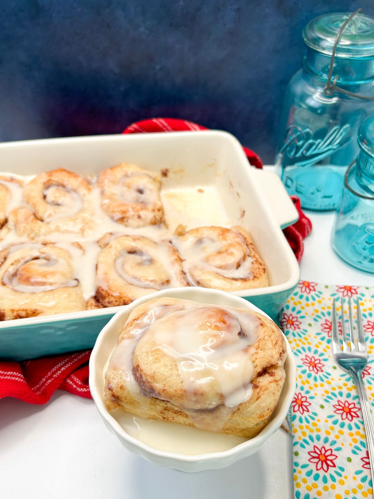 Big cinnamon rolls in a baking dish and one on a serving dish.