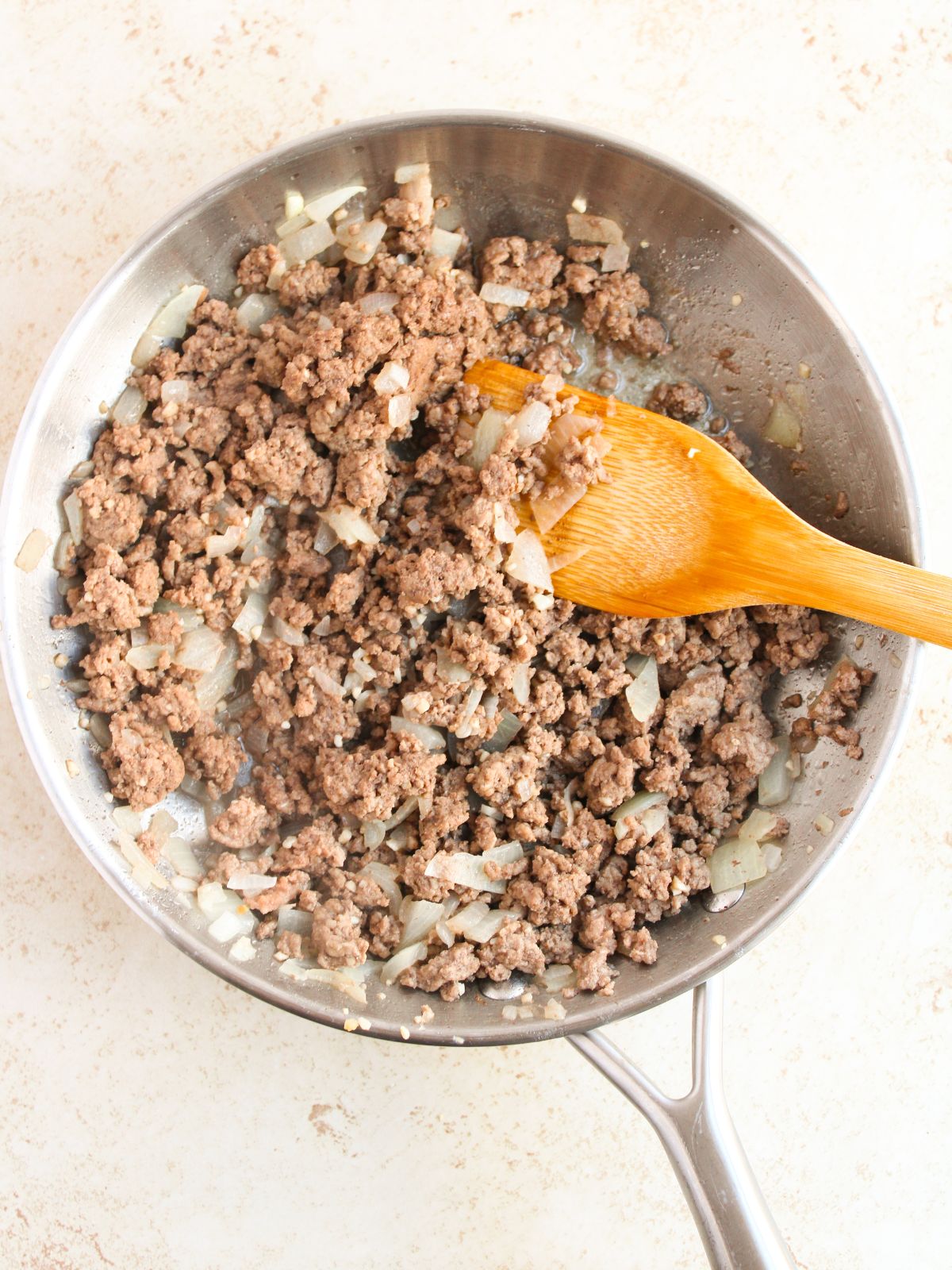 ground beef and onions in skillet with wooden spoon.