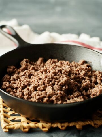 browned ground beef in cast iron skillet with kitchen towel in background.