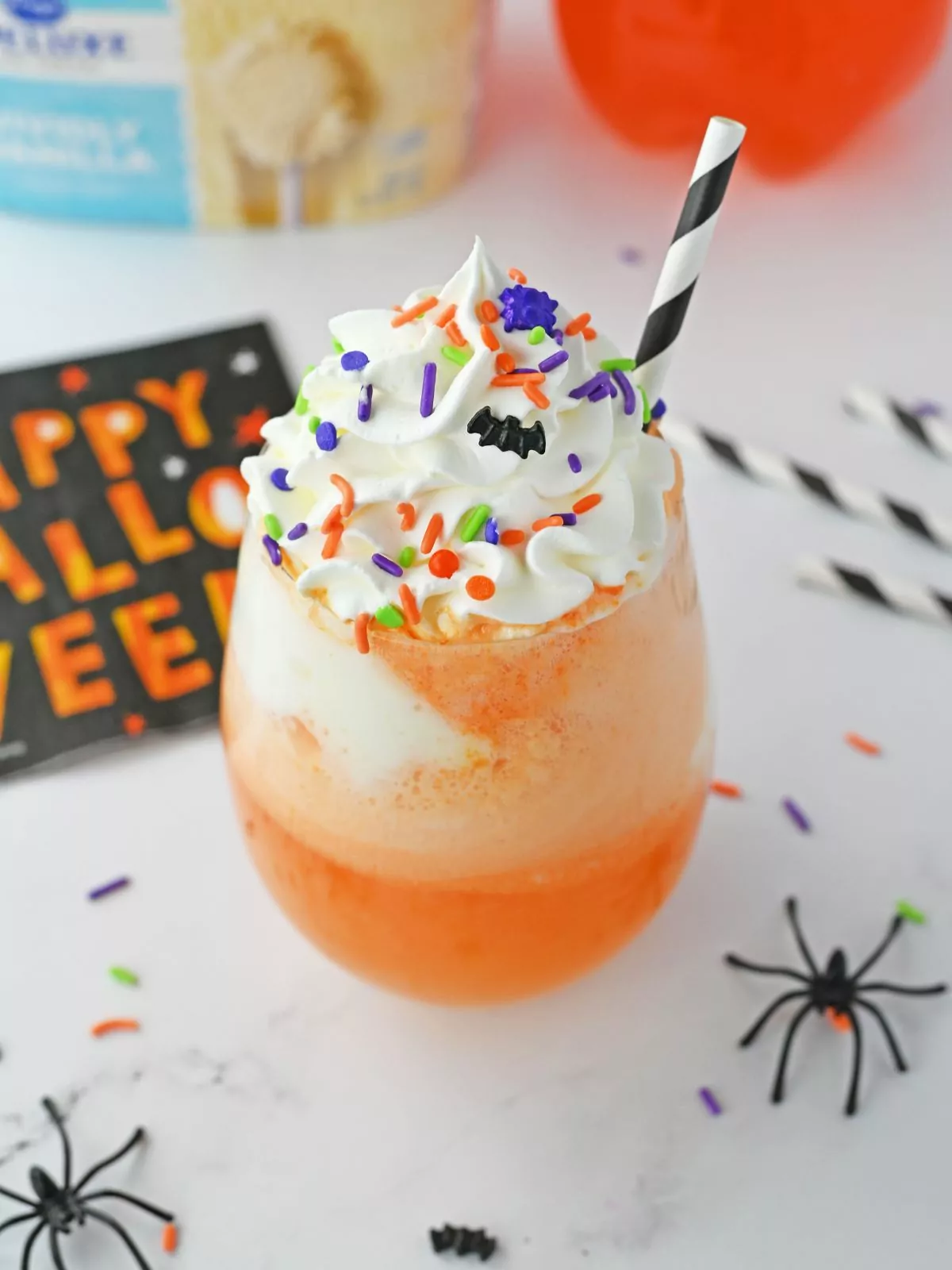 Halloween Punch for Kids. Orange punch with ice cream, whipped cream, Halloween sprinkles, and a black and white striped straw.