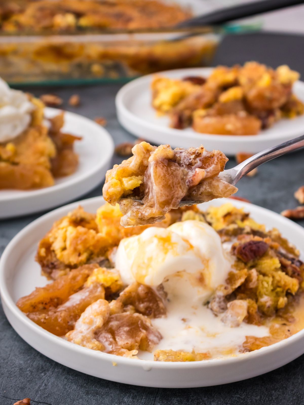 Forkful of apple cake lifted from a plate served with melty ice cream.