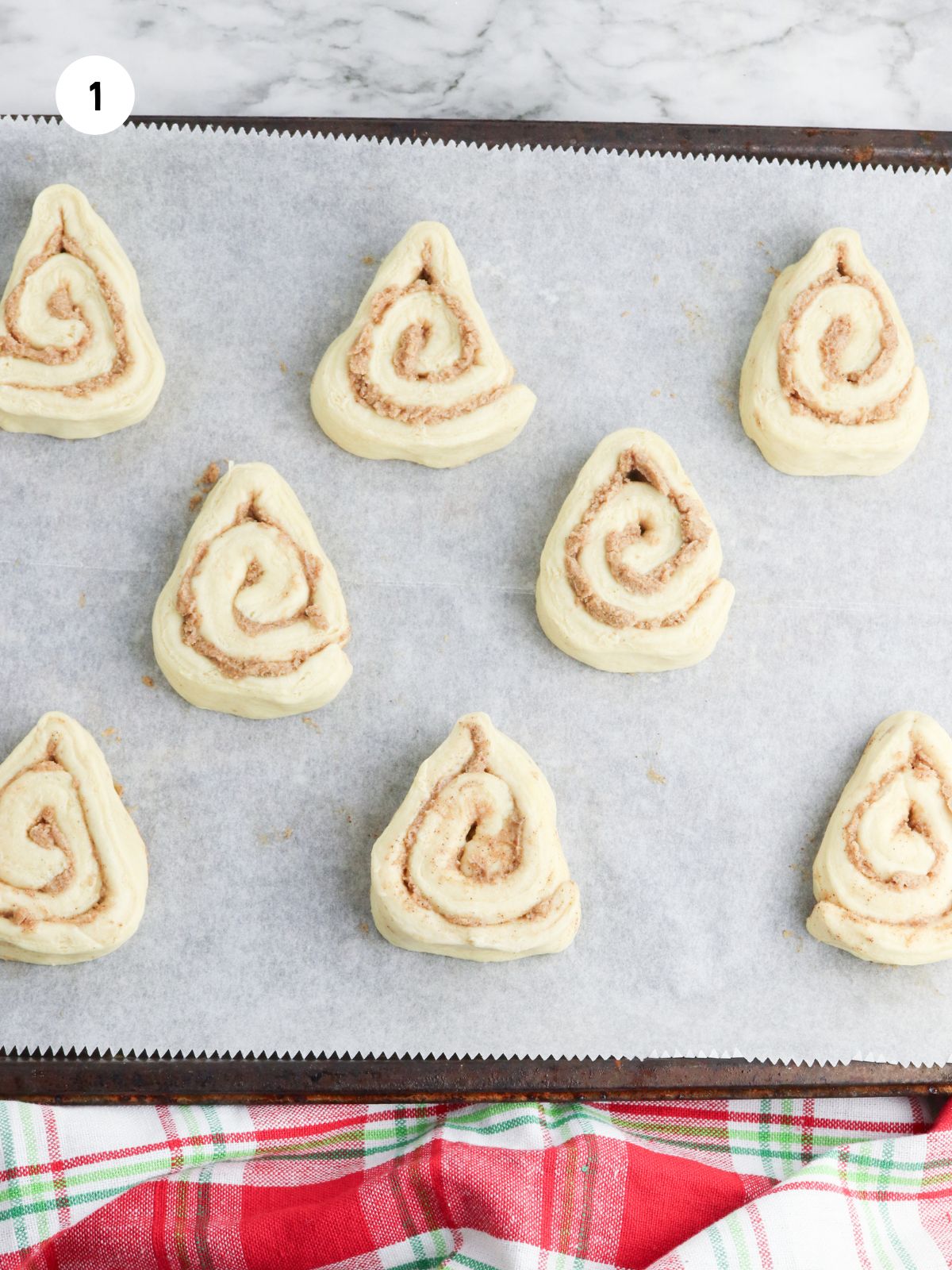 Cinnamon rolls shaped into triangles on a parchment lined baking sheet.