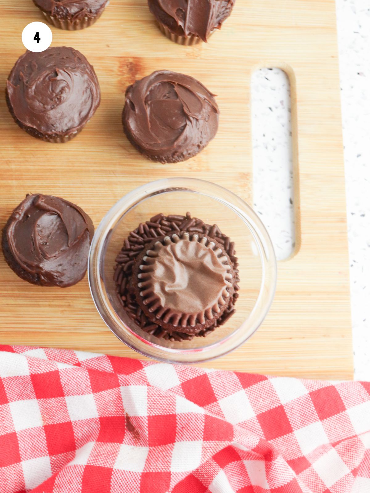 Frosted cupcake being dipped into a bowl of chocolate sprinkles.
