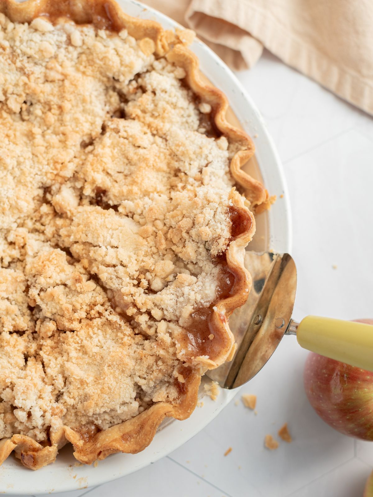 closeup of baked apple pie with crumb topping in pie plate with server.