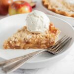 cloesup of apple pie with crumb topping and scoop of ice cream on plate with forks.