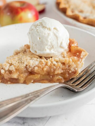 cloesup of apple pie with crumb topping and scoop of ice cream on plate with forks.