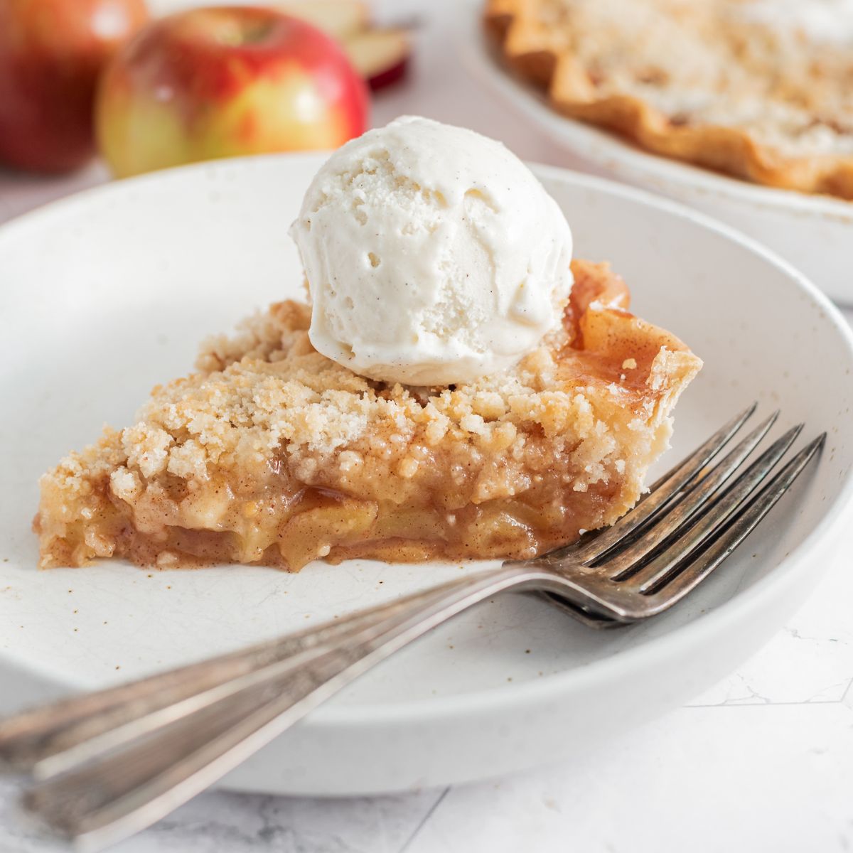 cloesup of apple pie with crumb topping and scoop of ice cream on plate with forks.