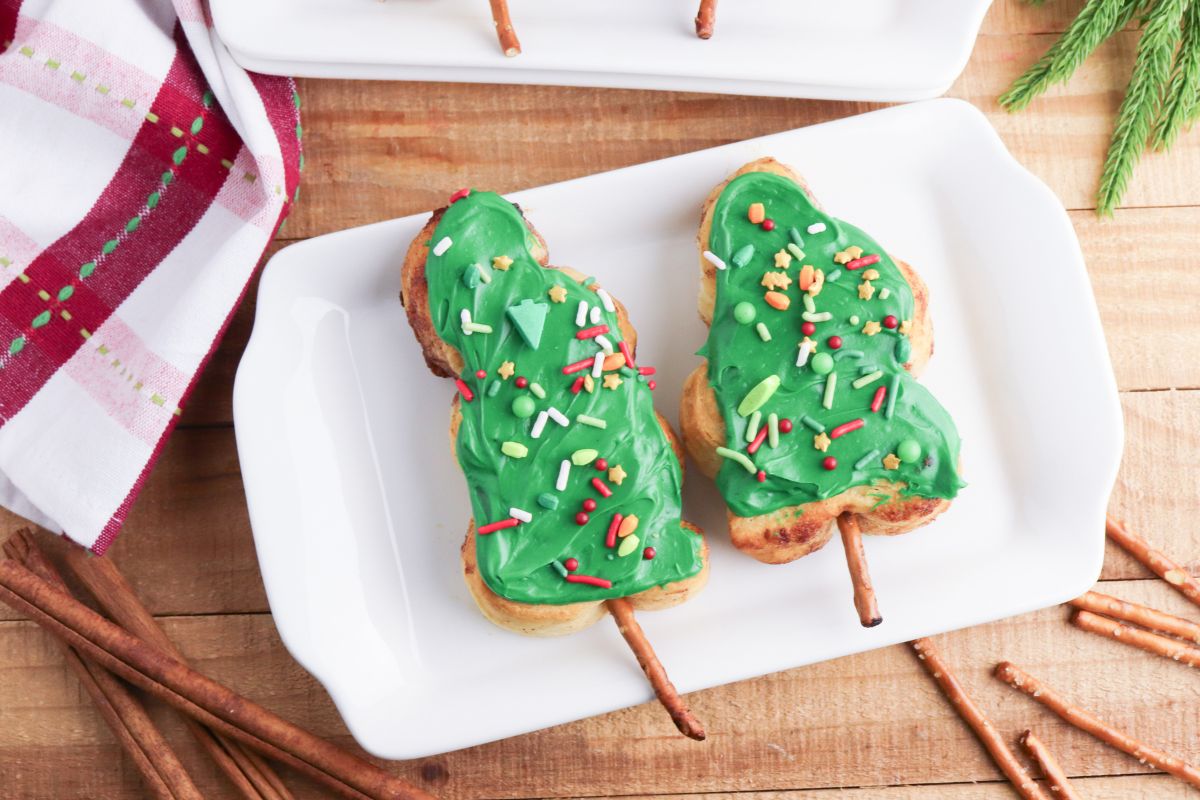 Two cinnamon rolls in a tree shaped frosted with green frosting and a pretzel stick trunk.