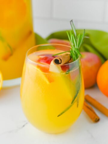 closeup of a sparkling cider drink with fall flavors or apples, oranges and cinnamon sticks.