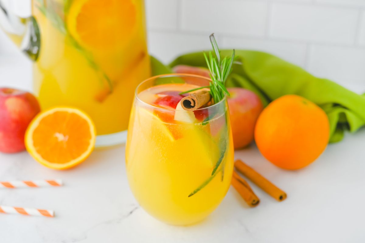 glass of beverage made with orange juice, apples, oranges, cinnamon sticks.