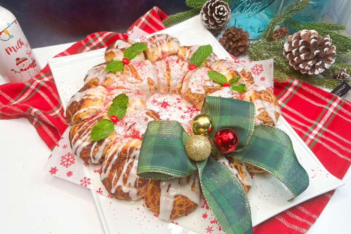 Christmas wreath made from refrigerated cinnamon rolls on platter with green bow.