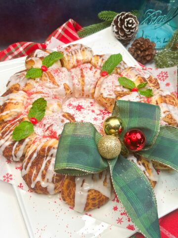 baked and decorated cinnamon rolls shaped into a wreath with green bow and ornaments.