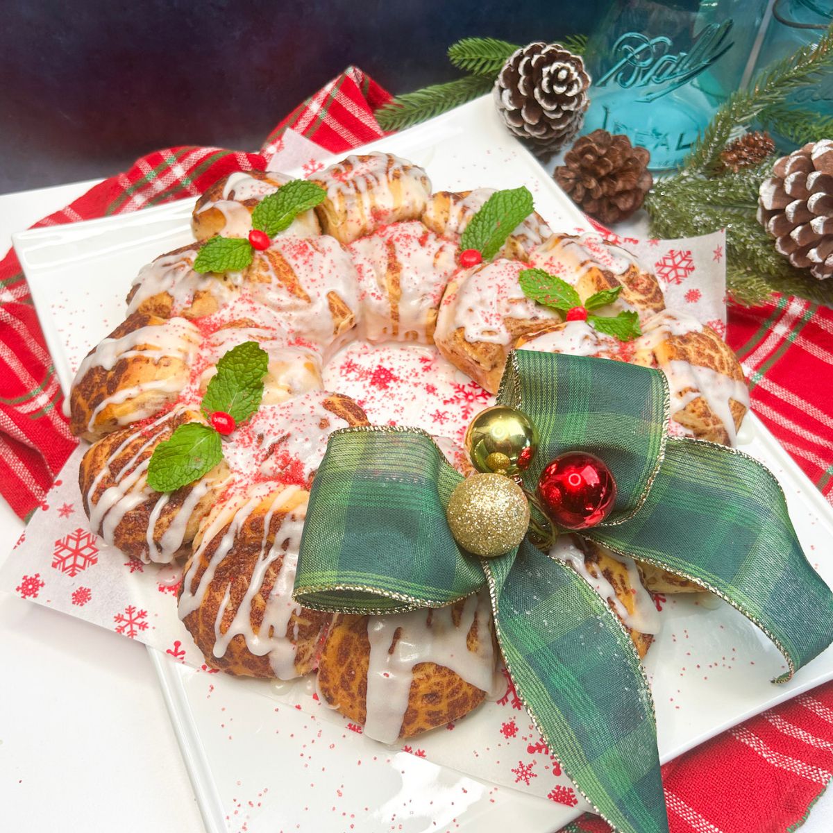 baked and decorated cinnamon rolls shaped into a wreath with green bow and ornaments.