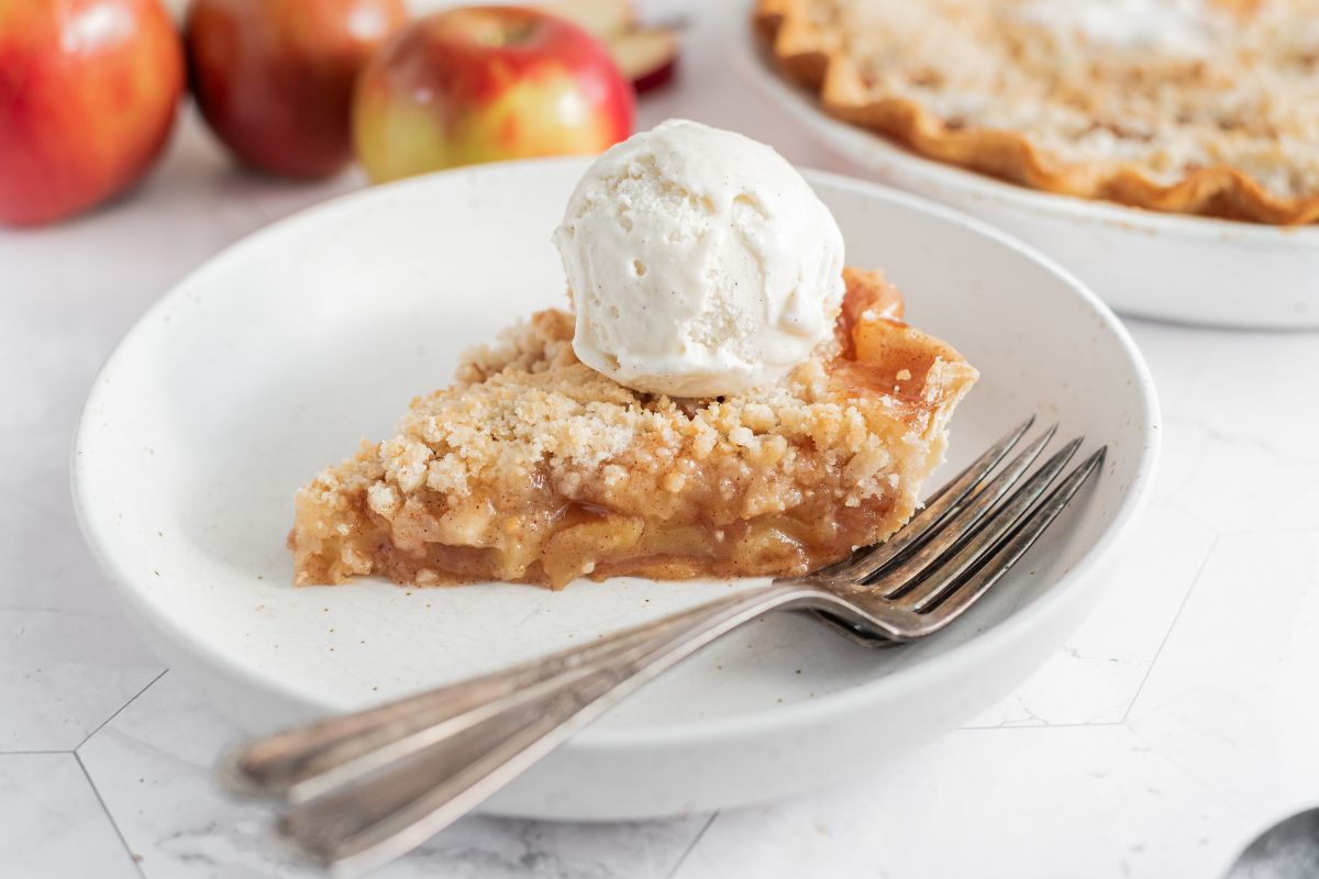 apple pie with crumb topping and scoop of ice cream on plate with forks.