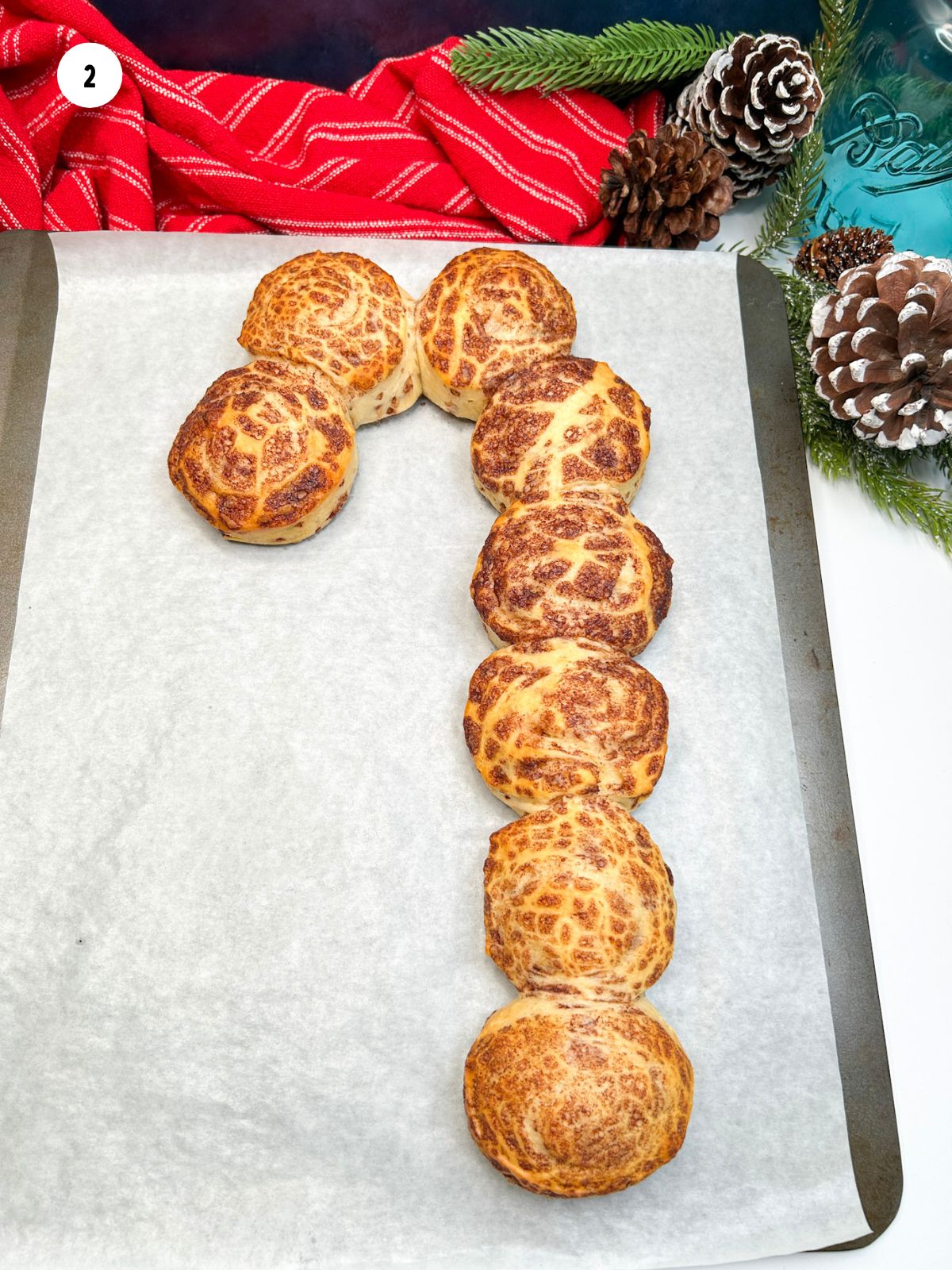 baked cinnamon rolls made into the shape of a candy cane on baking tray with parchment paper.