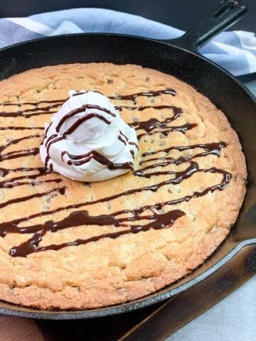 baked chocolate chip cookie in a cast iron skillet with scoop of whipped topping and chocolate sauce.
