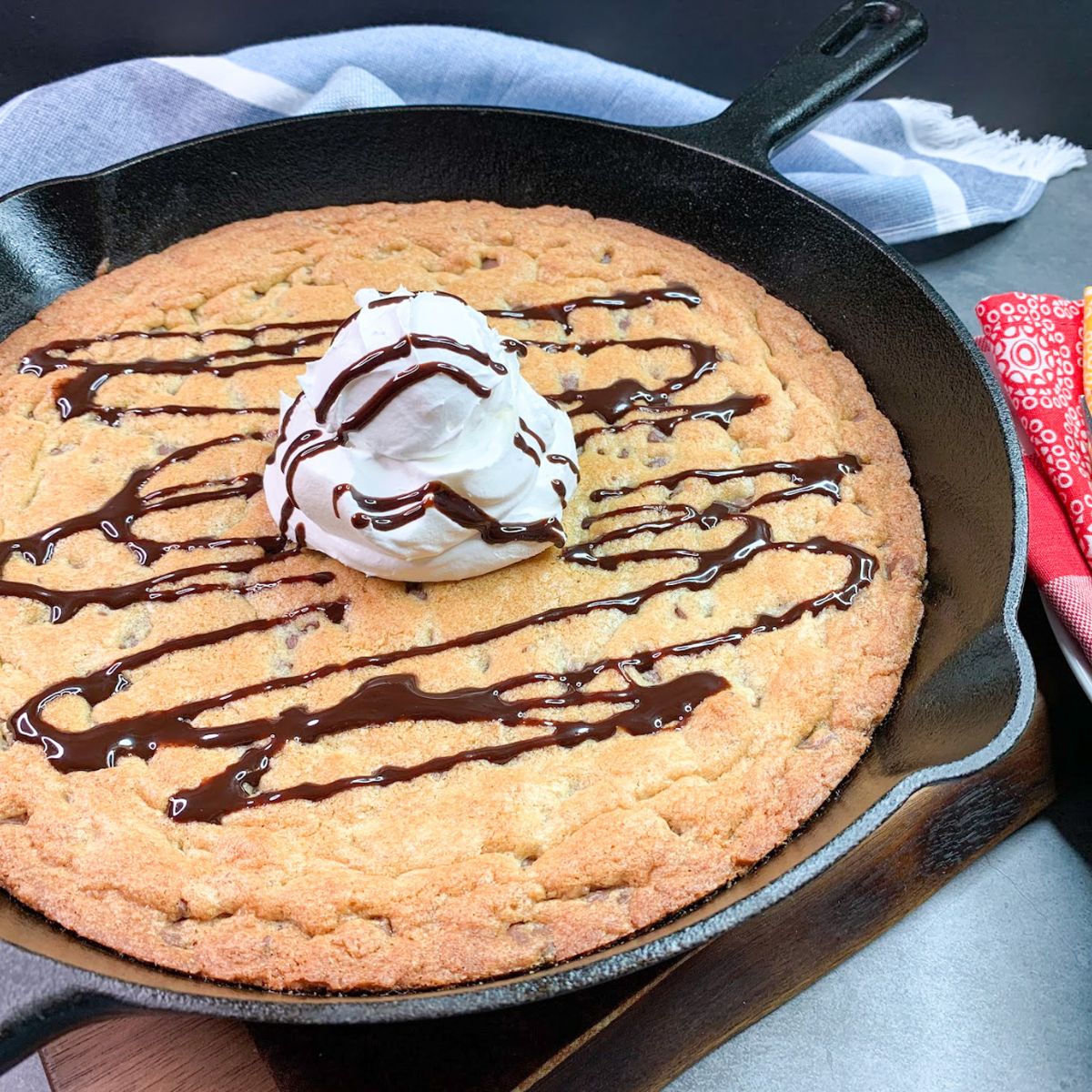 baked chocolate chip cookie in a cast iron skillet with scoop of whipped topping and chocolate sauce.