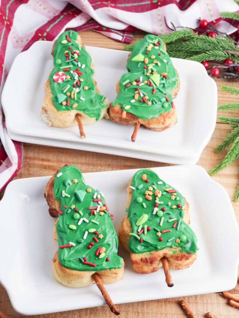 Two rectangle platters both with 2 cinnamon rolls decorated like Christmas trees.