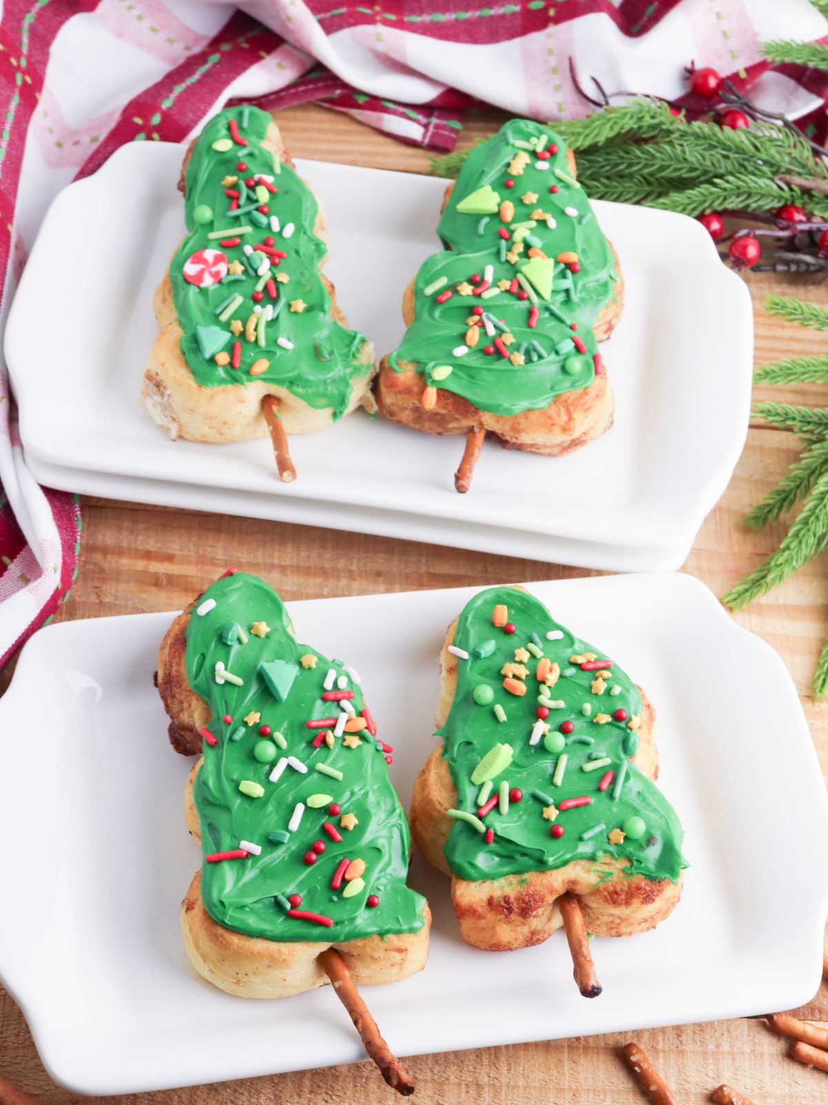 Two rectangle platters both with 2 cinnamon rolls decorated like Christmas trees.