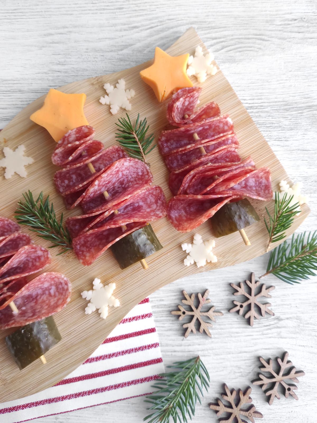 Christmas Tree Salami Appetizers on a board and wooden snowflakes scattered around.