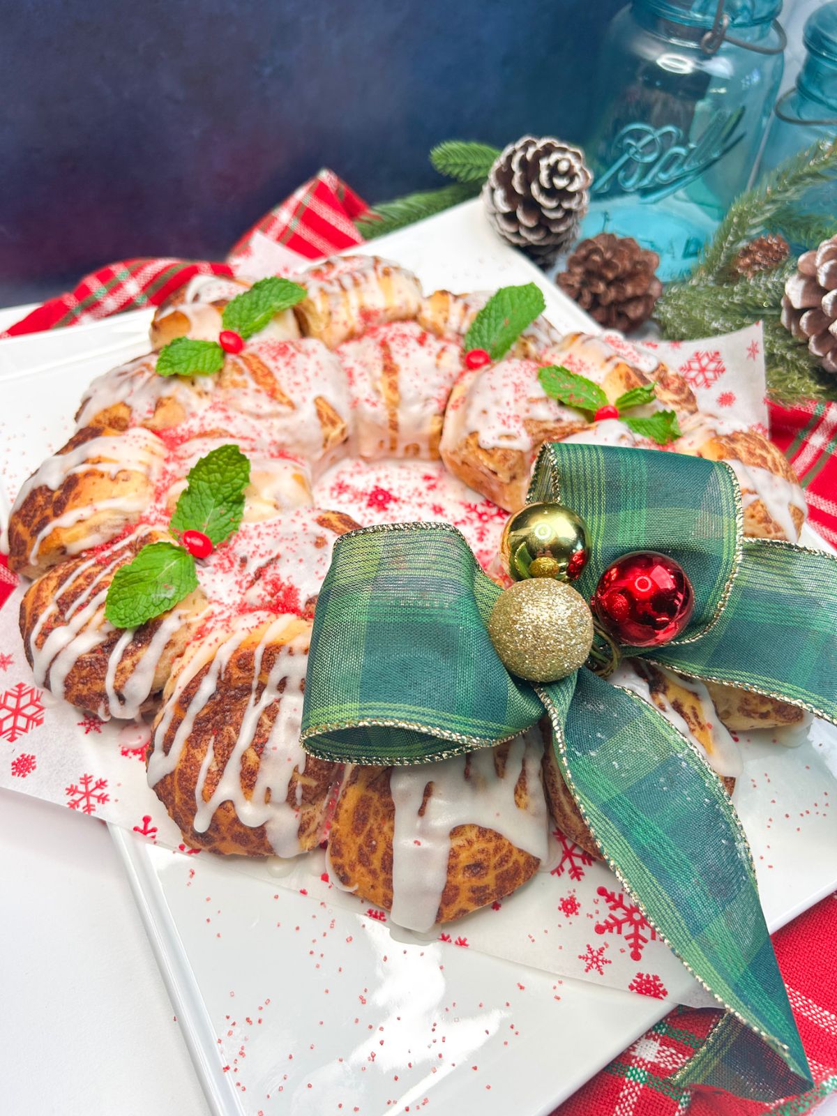baked and decorated Pillsbury cinnamon rolls shaped and decorated into a wreath on white plate.