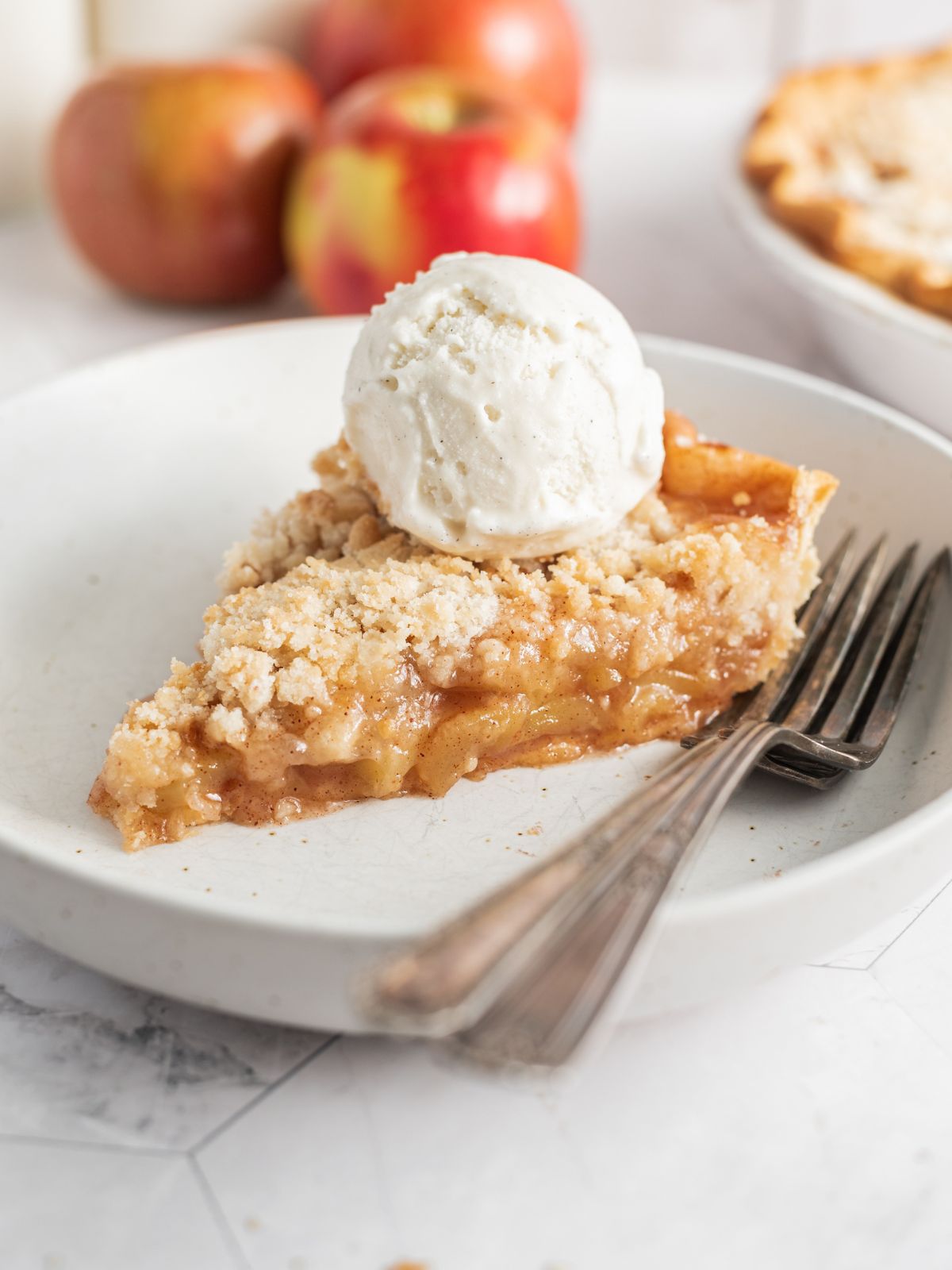 closeup photo of apple crumb pie with scoop of ice cream on plate with forks.