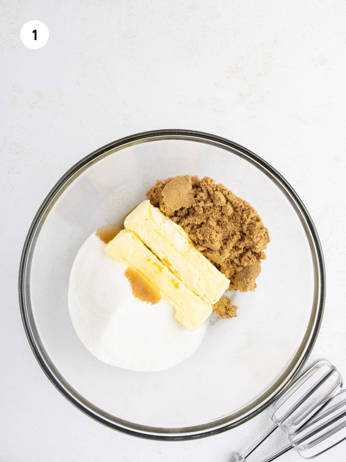 Clear mixing bowl with brown and white sugars, butter, and vanilla.