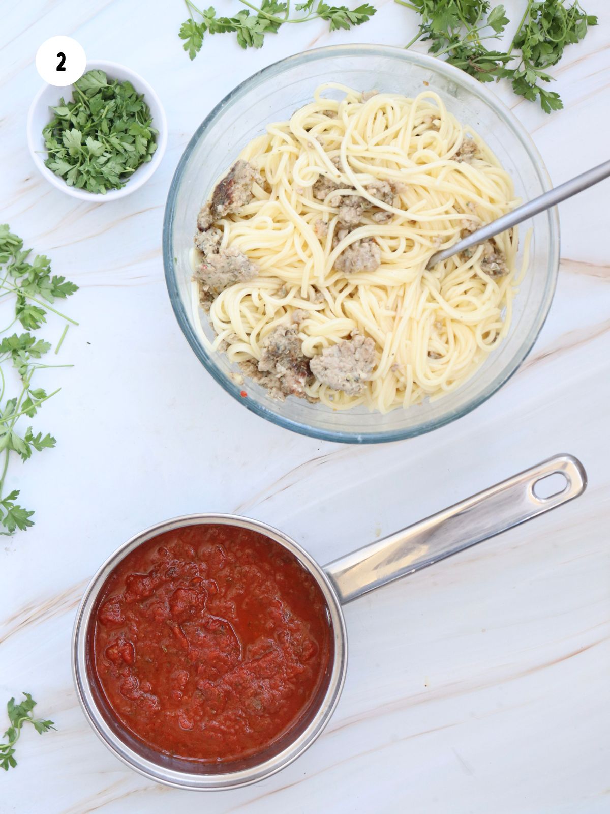 Bowl of cooked spaghetti and Italian sausage. Small pot of spaghetti sauce.