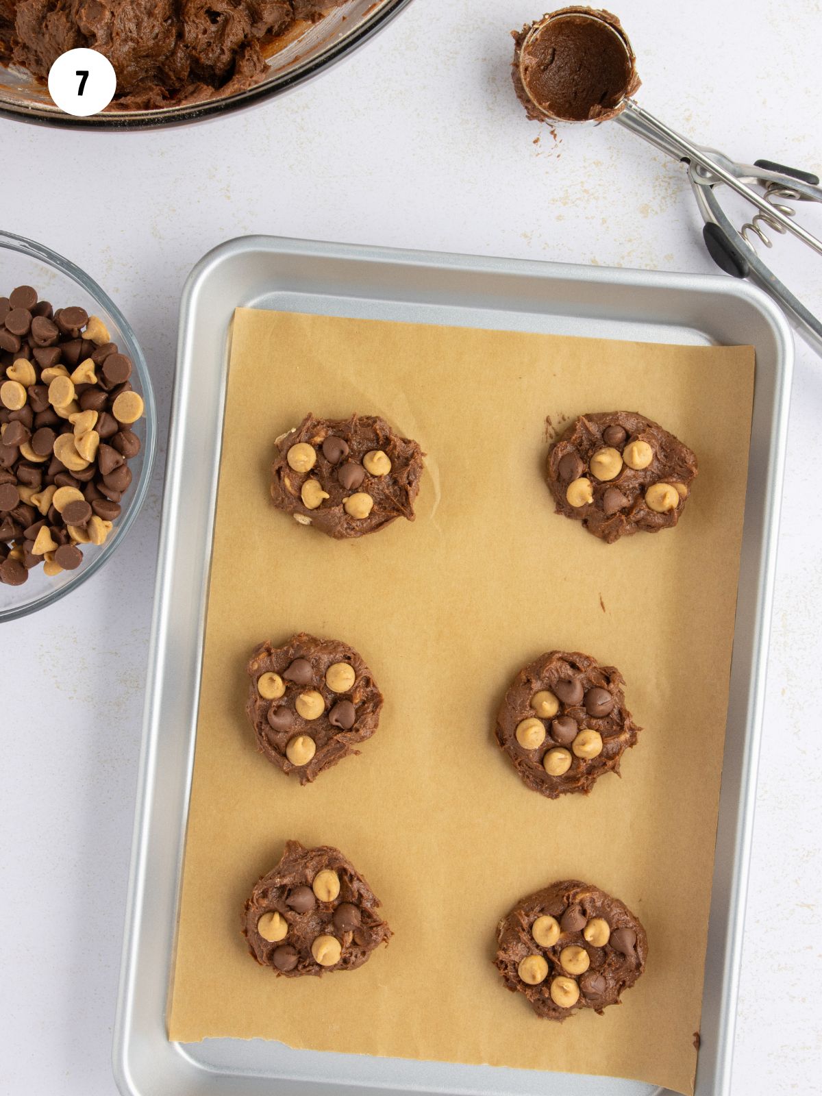 Scooped out cookie dough on a parchment lined baking sheet. Additional chocolate and peanut butter chips added to the tops.