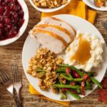 Overhead view of a classic Thanksgiving dinner plate with turkey, stuffing, mashed potatoes and gravy, green beans, and cranberry sauce for a simple Thanksgiving recipe menu.