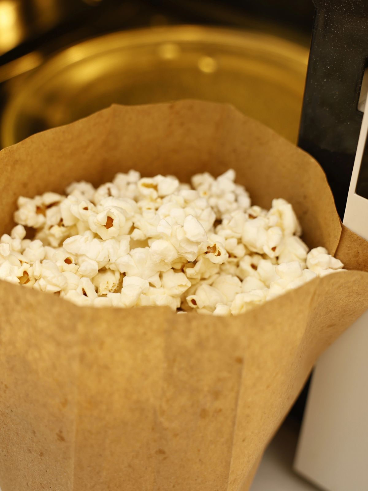 closeup of popped popcorn in paper bag with microwave in background.