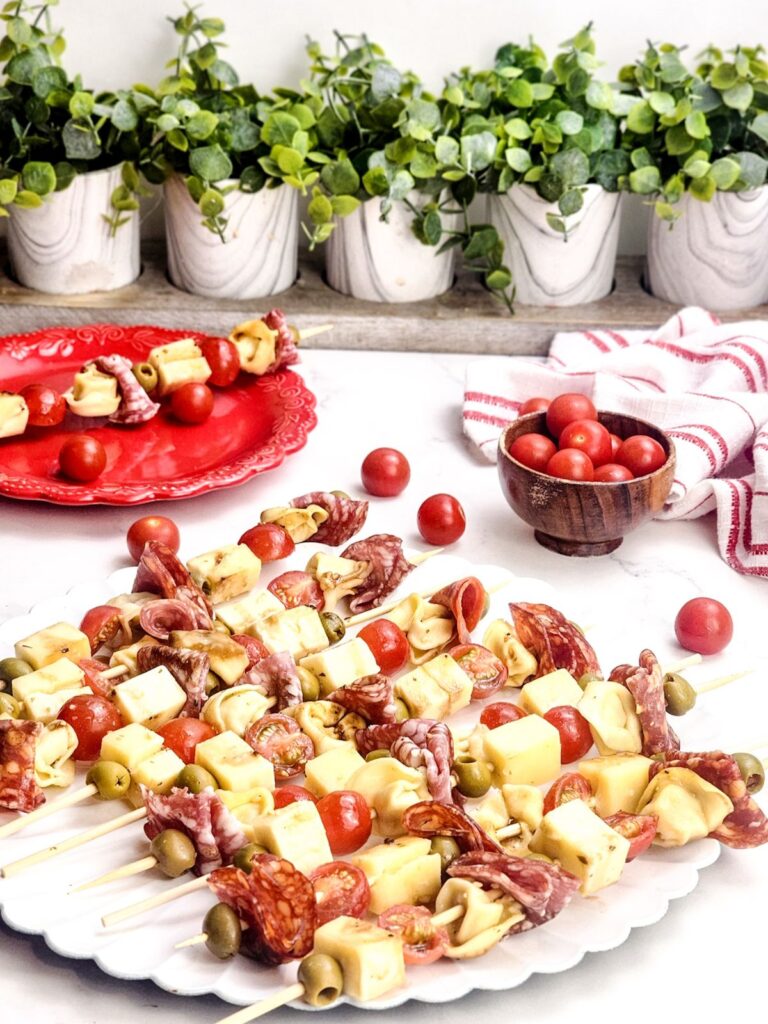 Scalloped edged white platter filled with antipasto skewers.