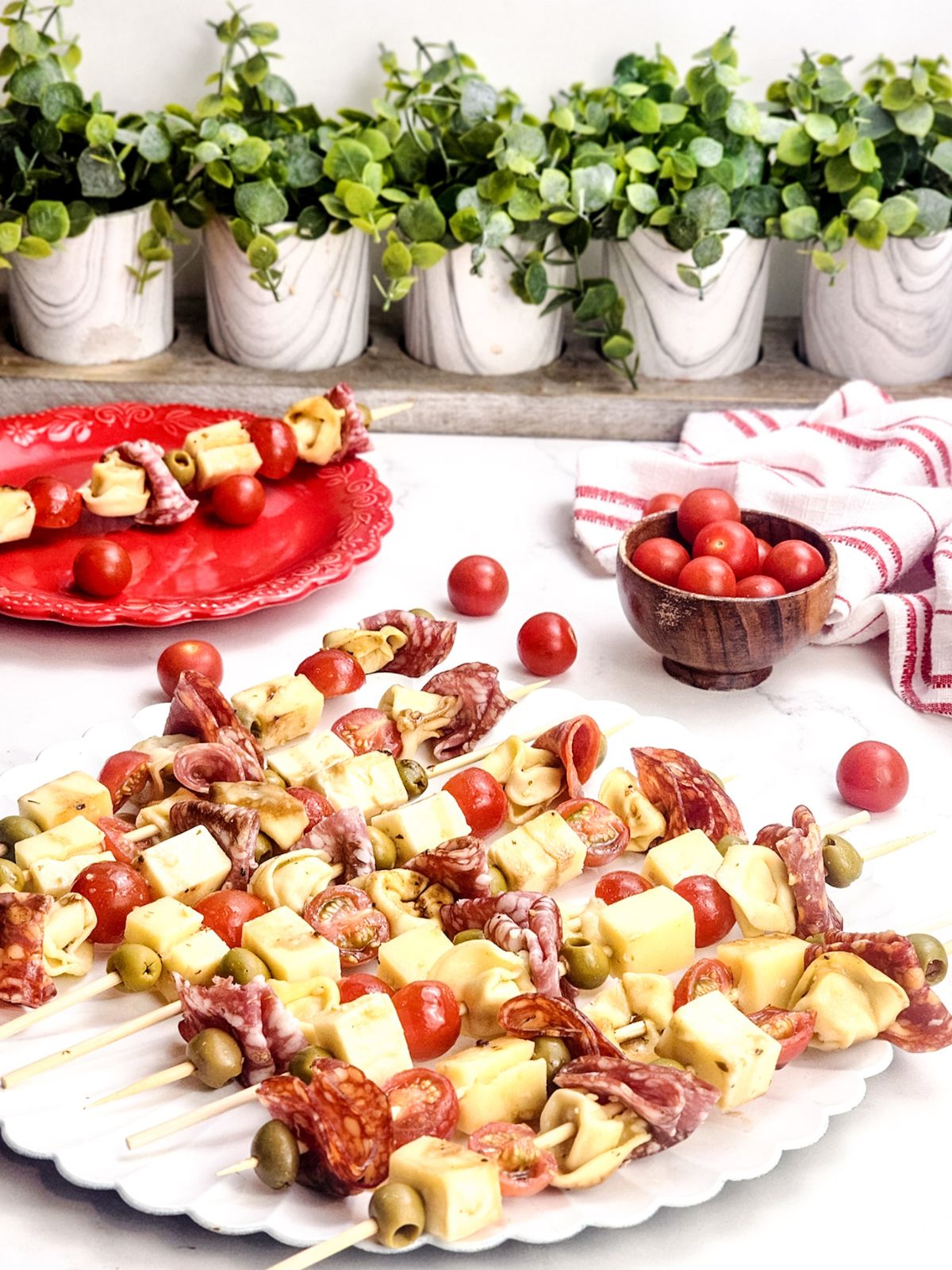 Scalloped edged white platter filled with antipasto skewers.