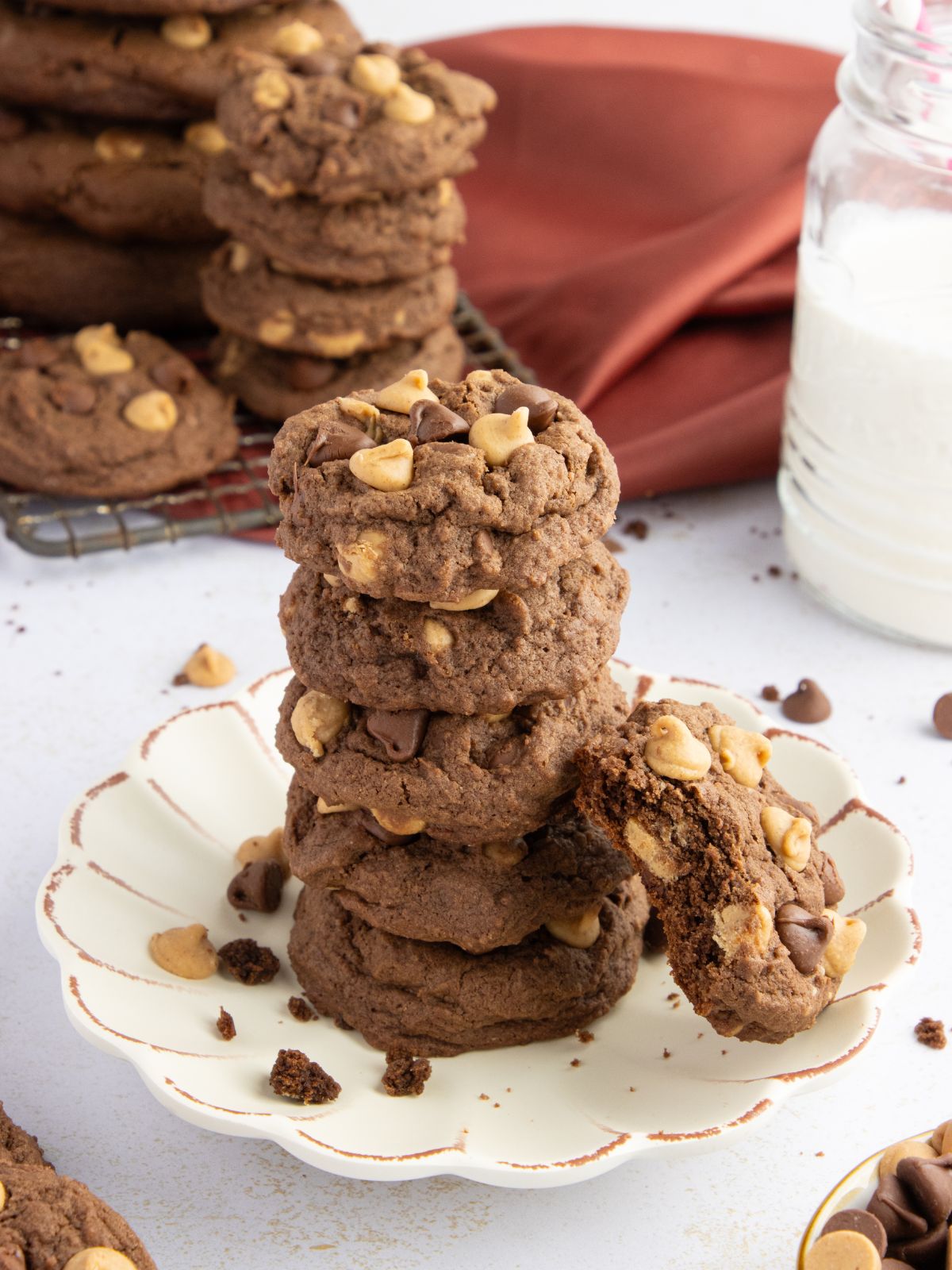 Stack of chocolate cookies with peanut butter chips and chocolate chips on a scalloped edge white plate.