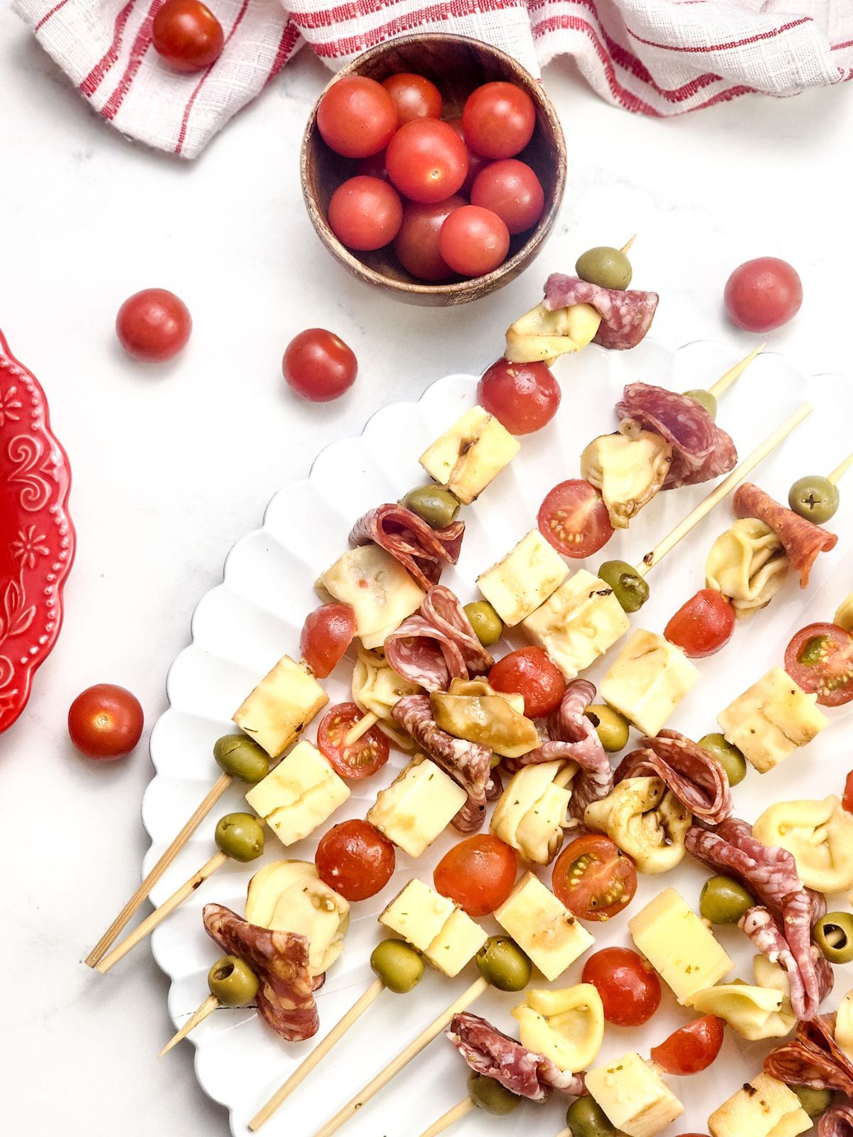 antipasto skewers on a scalloped edged platter and a small bowl of cherry tomatoes.