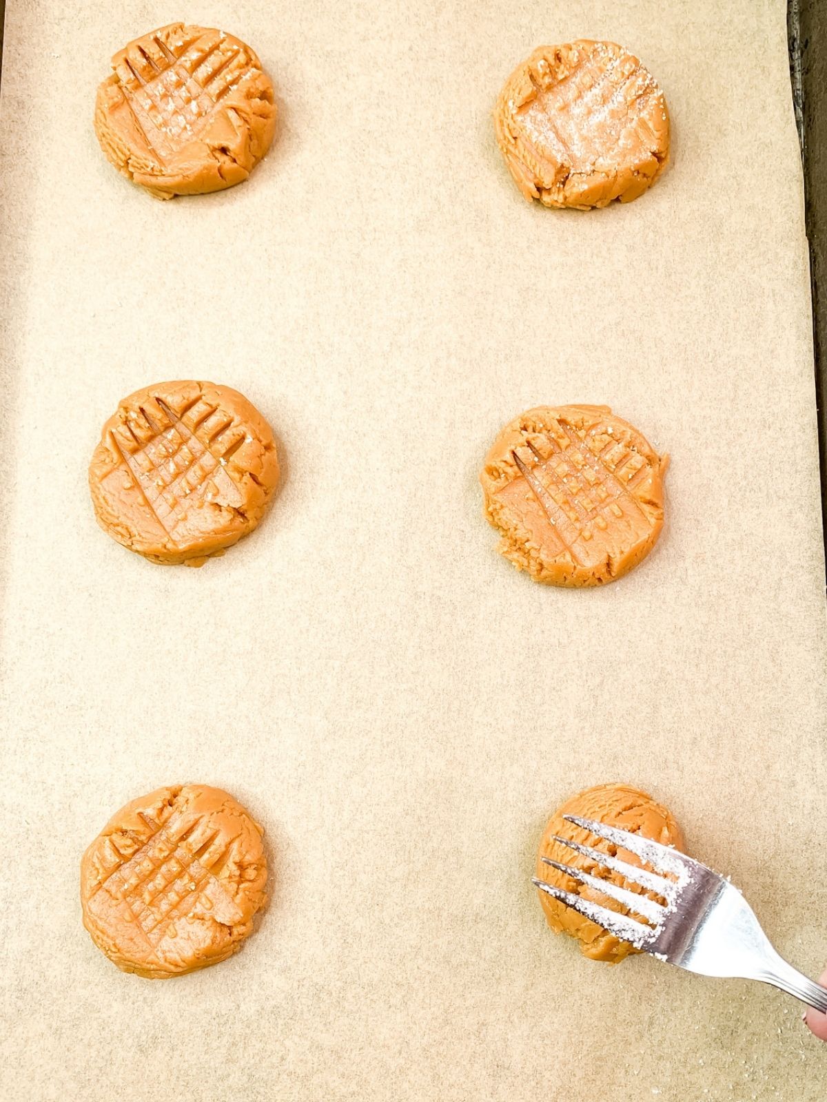 peanut butter cookie dough balls being flattened and crisscrossed with a fork.
