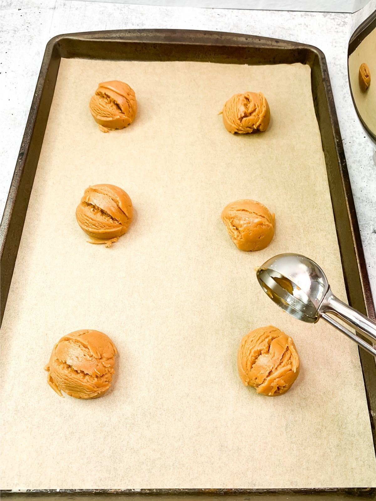 baking tray with parchment paper and cookie dough balls and cookie scoop.