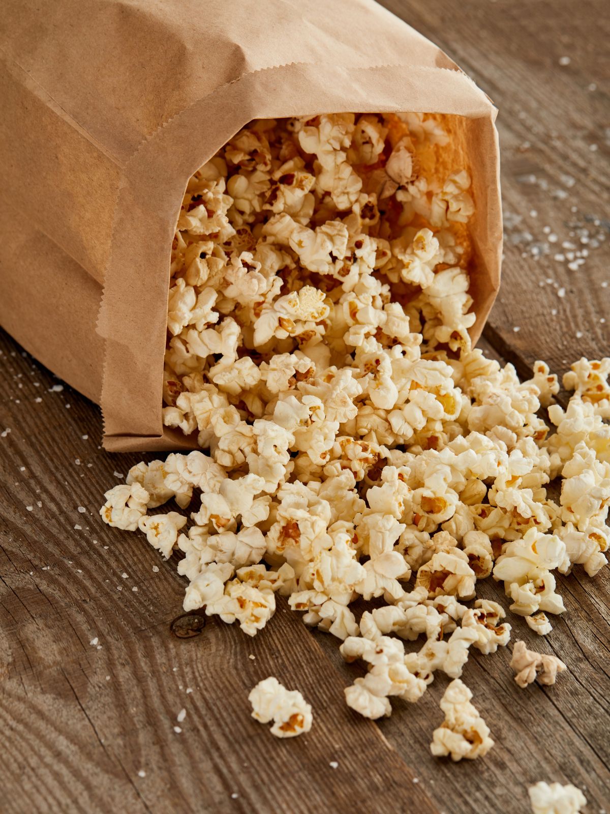 popcorn spilling out of a paper bag on a wooden board.