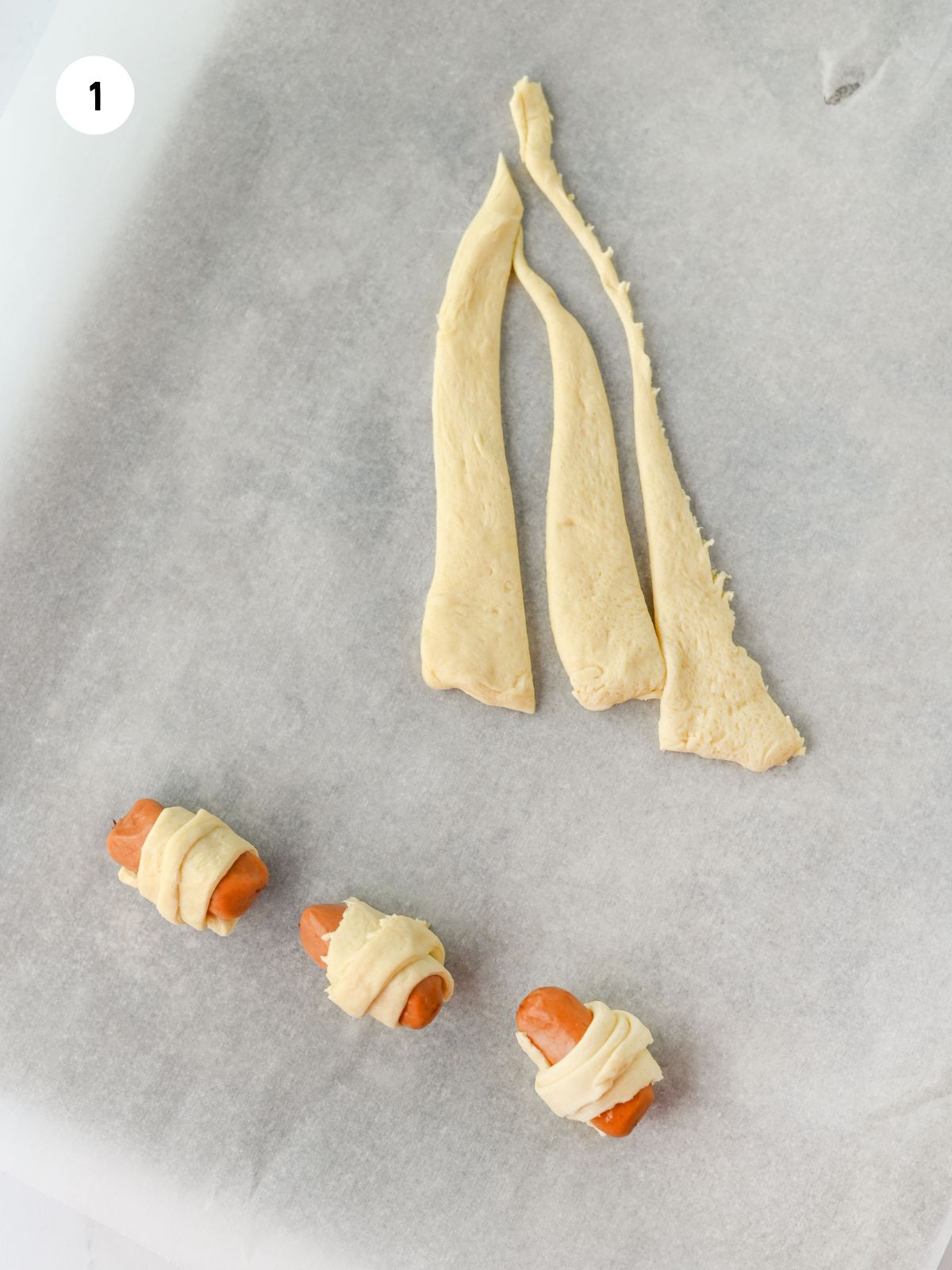 Crescent triangle cut in to 3 strips and 3 sausages wrapped in crescent dough.