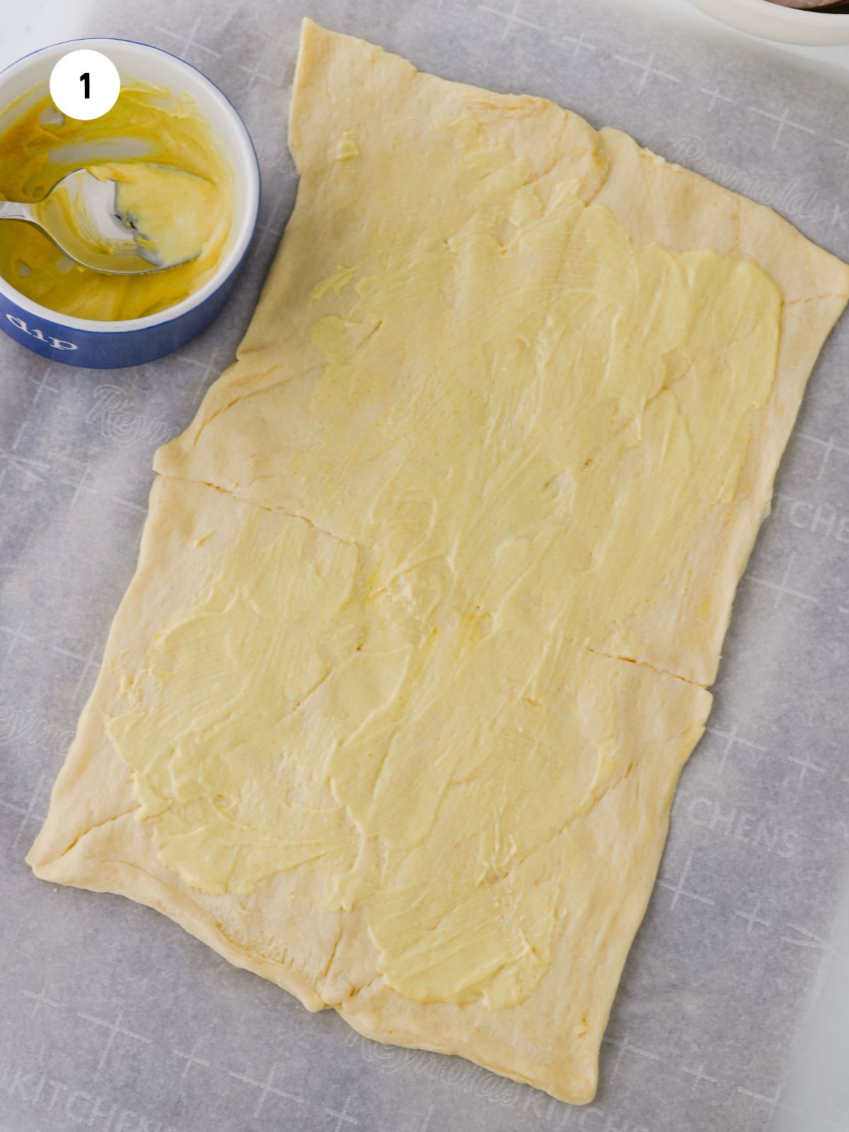 Mustard and mayo spread on a sheet of crescent roll dough.