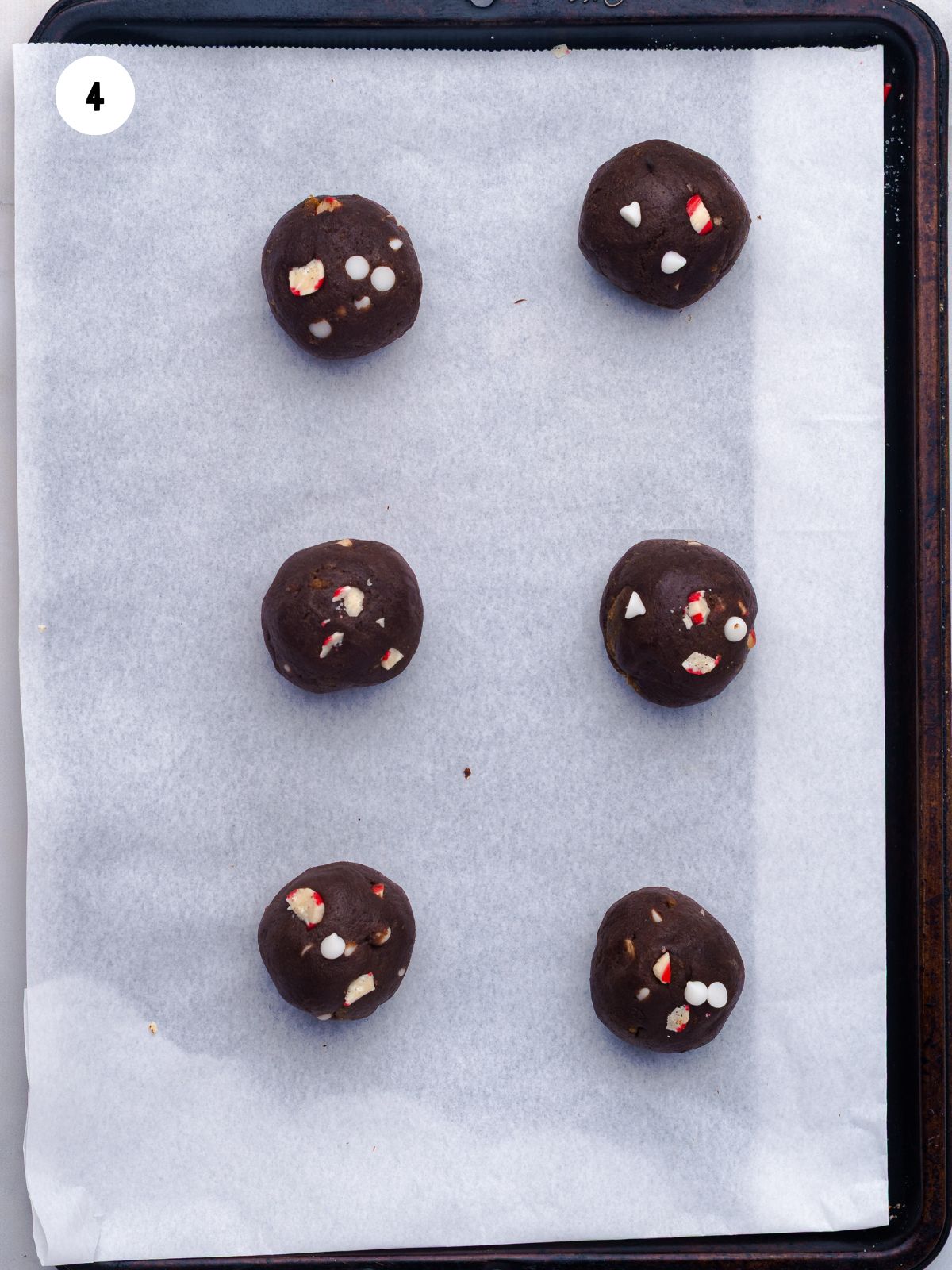Six scoops of cookie dough on parchment lined baking sheet.