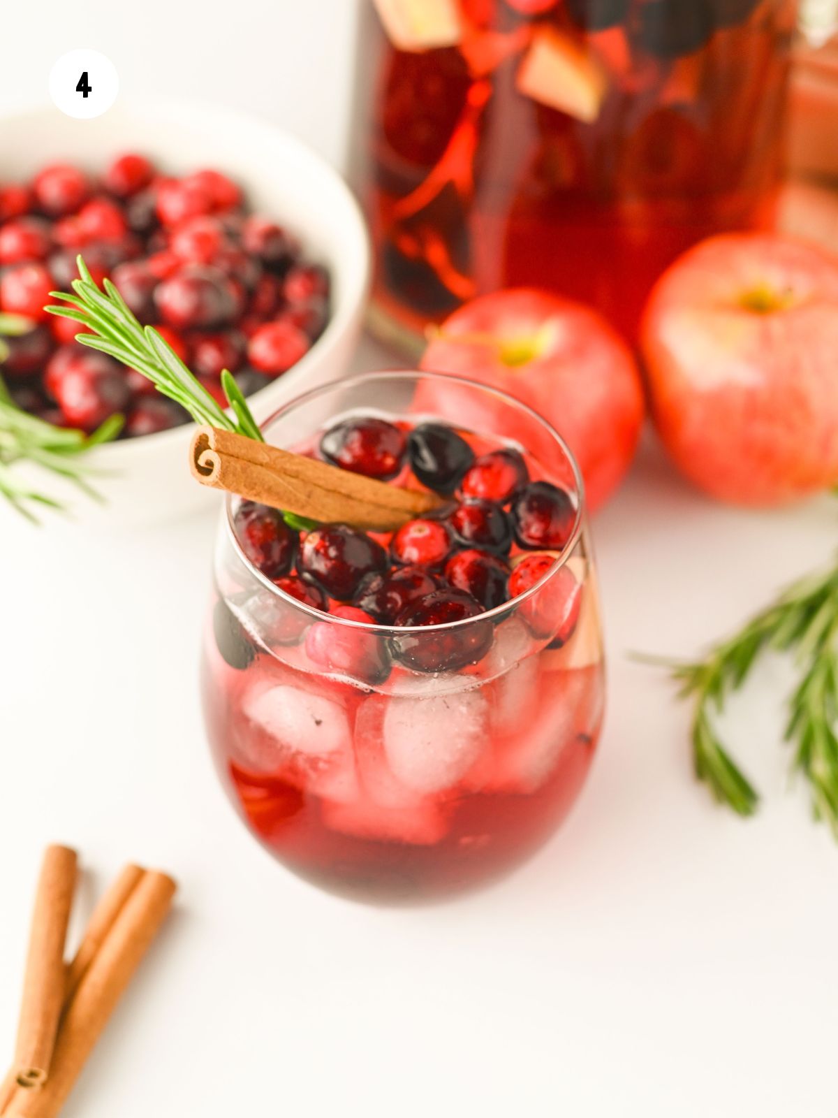 Glass of non alcoholic Christmas cranberry punch garnished with fresh cranberries, cinnamon sticks, and a sprig of rosemary.