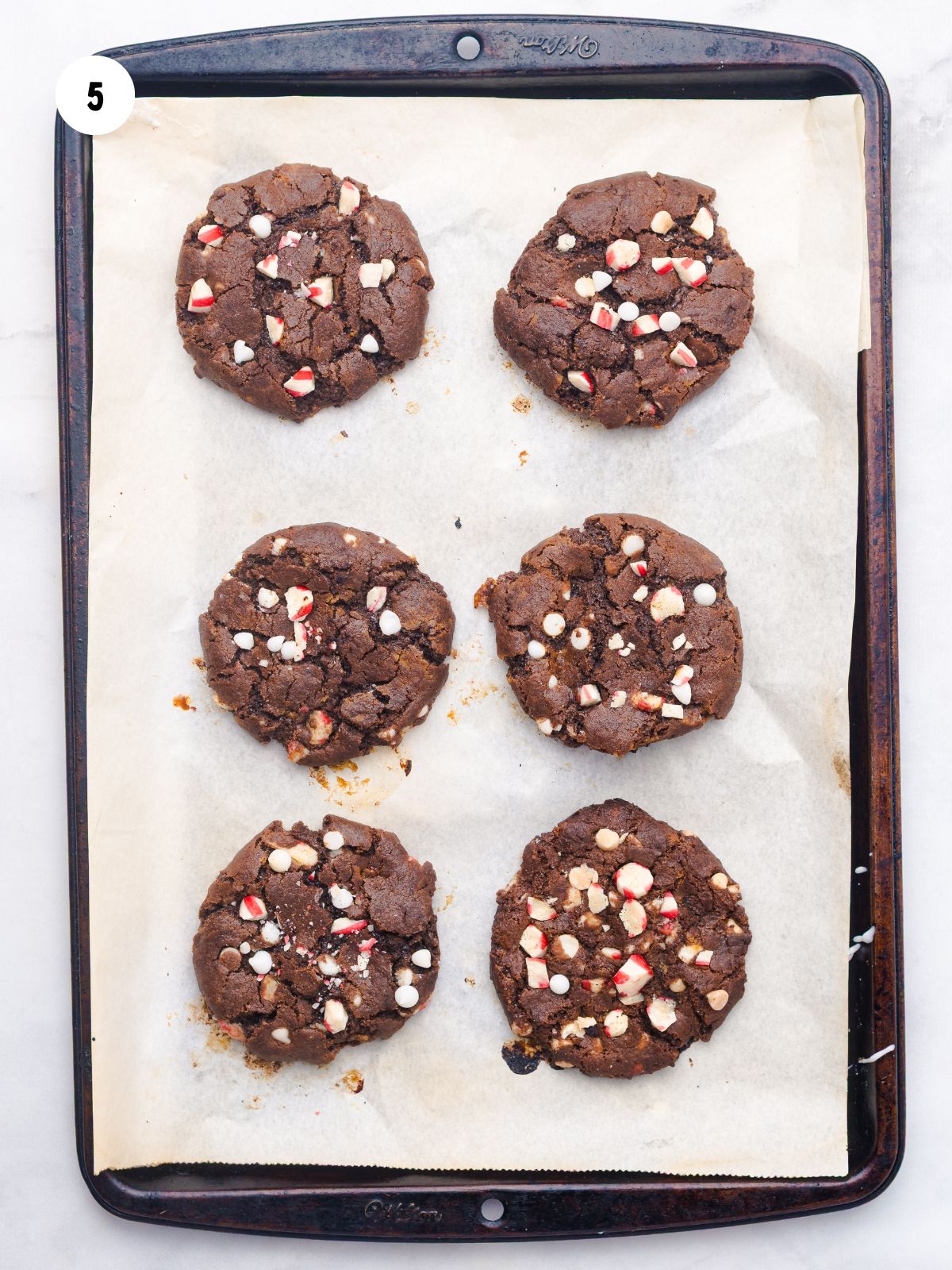 Six baked Chocolate Peppermint Cookies on a parchment lined baking sheet.