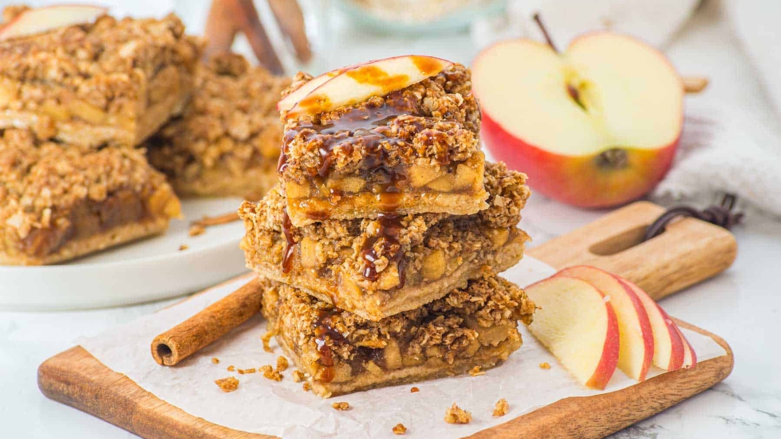 Three stacked apple crumble bars topped with a fresh apple slice, drizzled with caramel sauce.